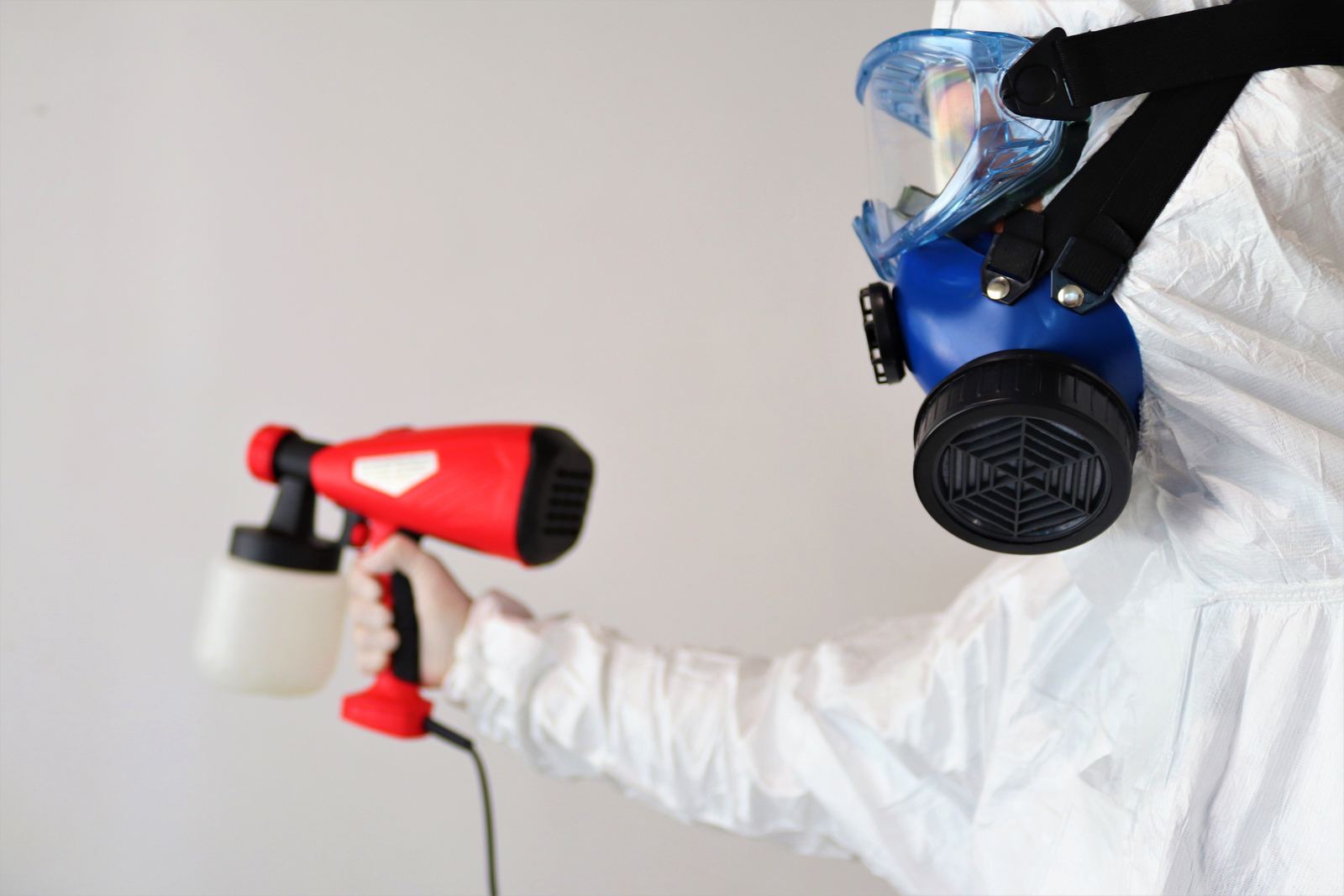 Technician in a protective suit and respirator applying treatment with a sprayer during mould remediation work