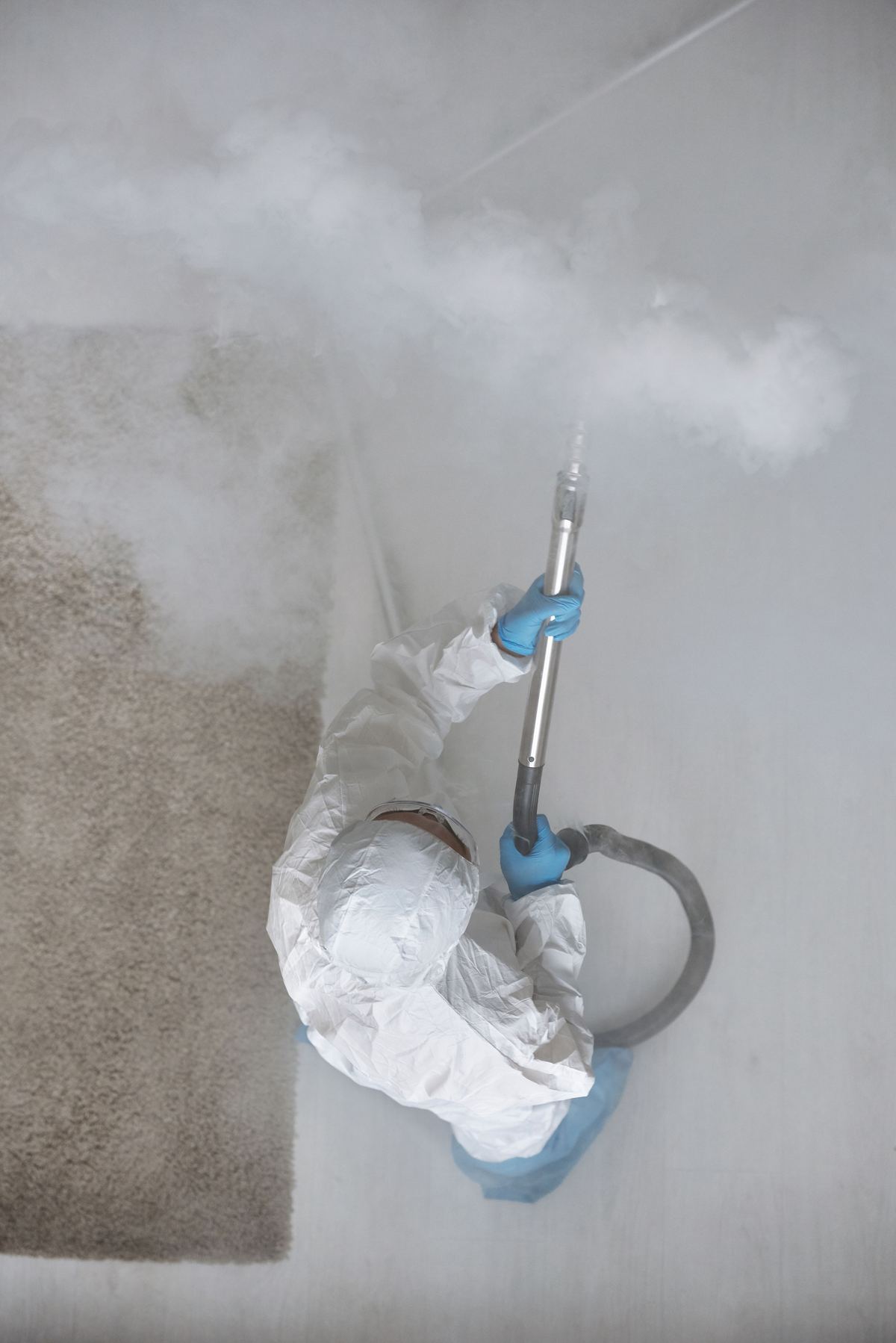 Technician in protective equipment treating wet carpet with steam equipment during a water-damage response